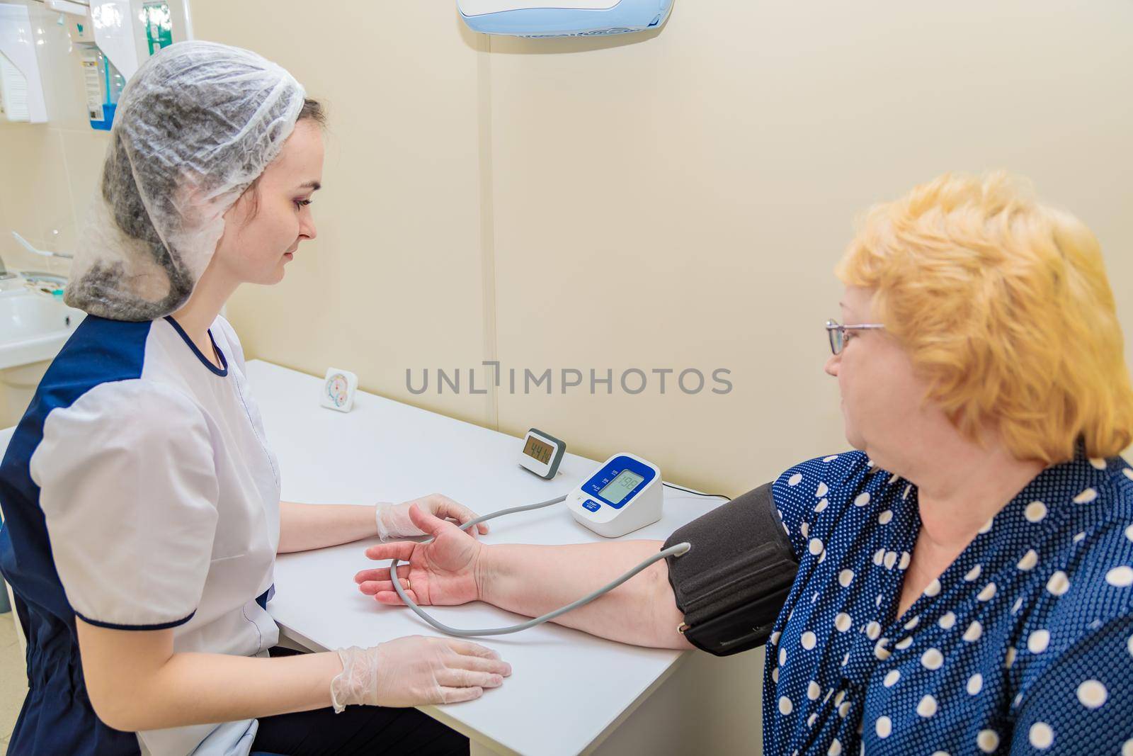 A nurse in a polyclinic measures the blood pressure of a woman with a device. Healthcare by Yurich32