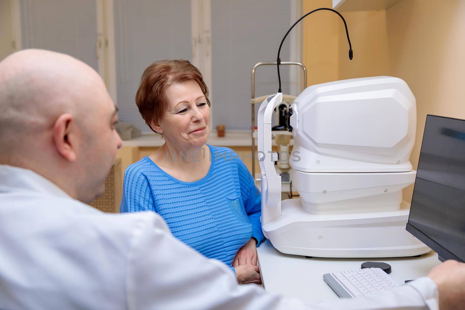 A male ophthalmologist explains the results of an eye examination to an adult woman, showing a drawing on a computer.