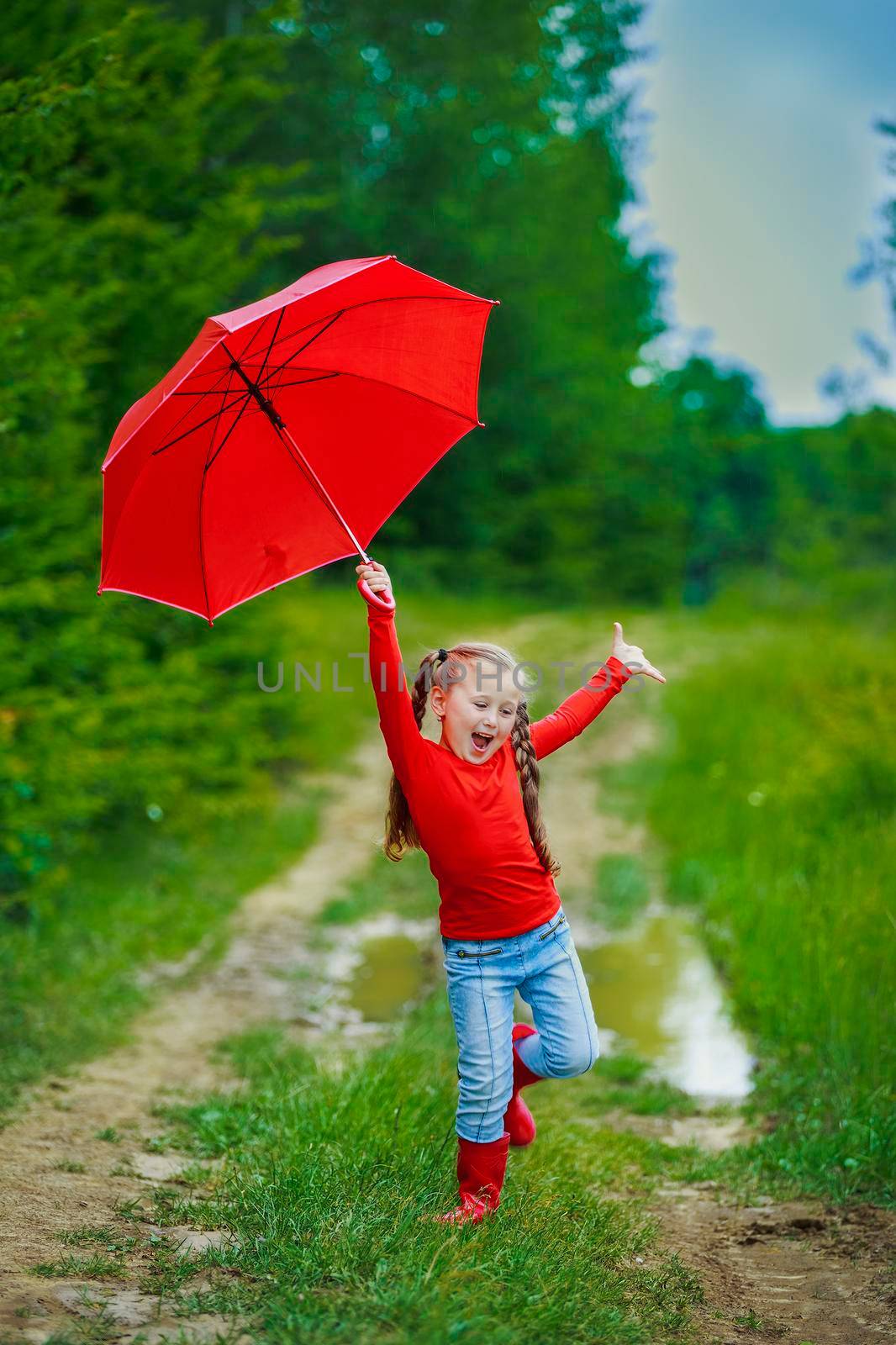girl with a red umbrella walking on a dirt road