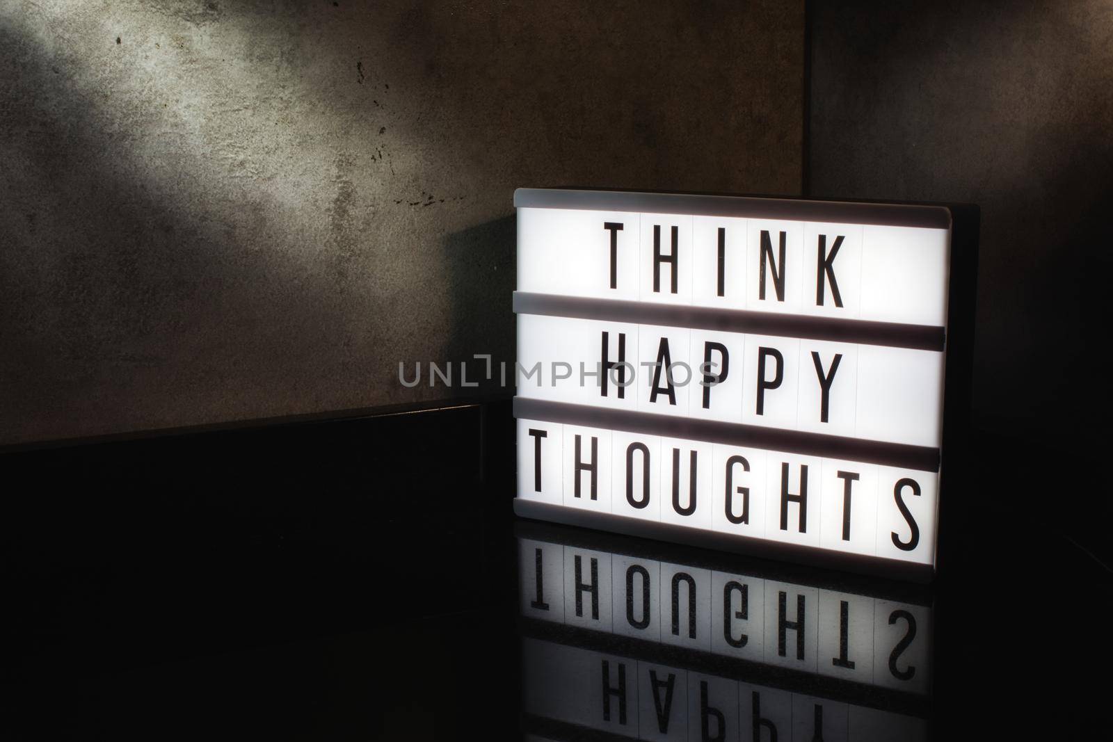 Think happy thoughts motivational message on a light box in a cinematic moody background