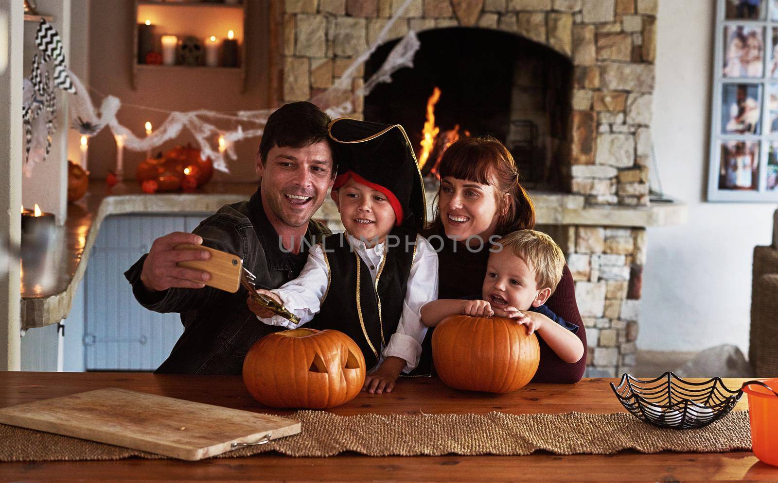 These special moments deserve to be captured. Shot of an adorable young family taking selfies together with a cellphone on halloween at home. by YuriArcurs