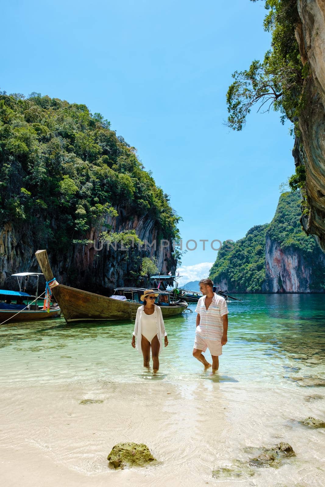 Koh Lao Lading near Koh Hong Krabi Thailand, beautiful beach with longtail boats, a couple of European men, and an Asian woman on the beach.