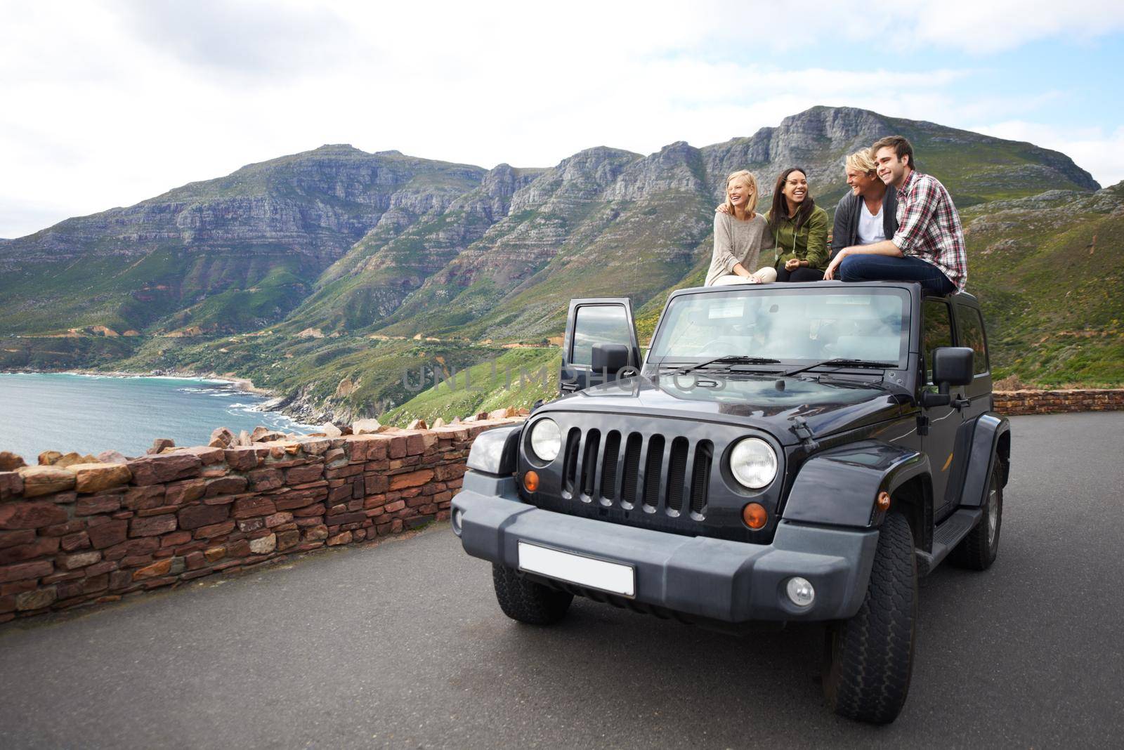 Shot of a group of friends relaxing on the roof of their truck with a mountainous background.