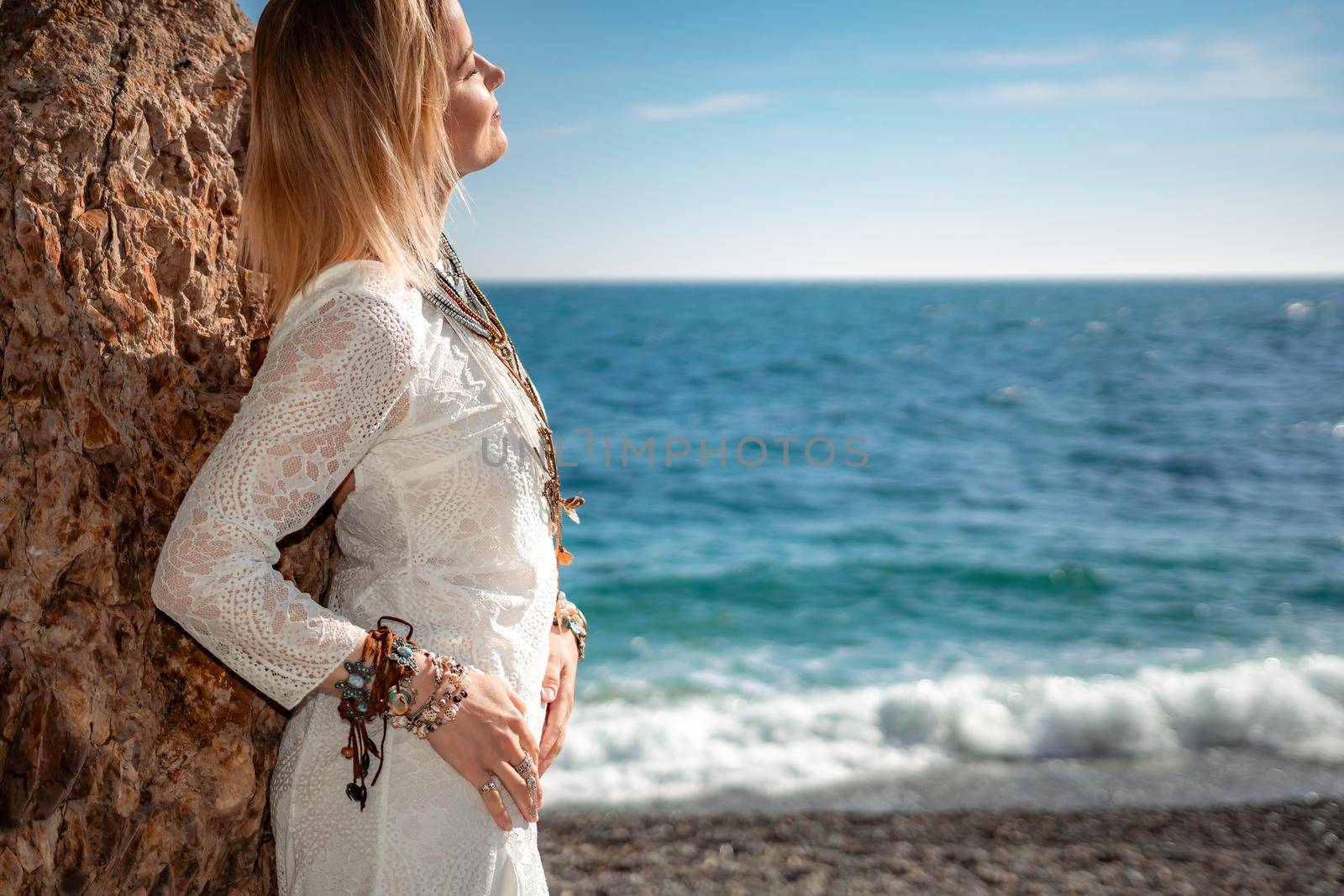 Woman in bohemian clothing on beach at sunset. Boho style for fashionable look on resort. Middle aged well looking woman in white dress and boho style braclets. Summer fashion by panophotograph