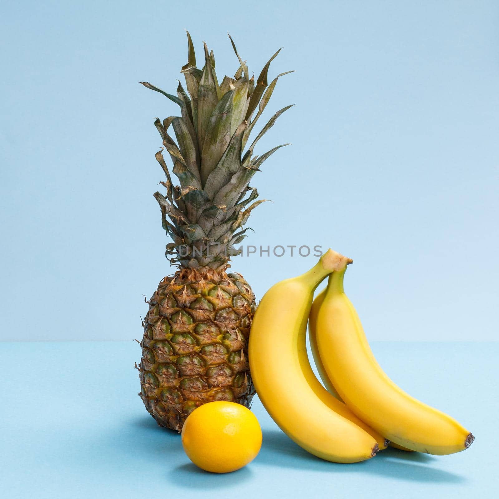 Natural composition with tropical fruits. Fresh pineapple, bananas and a lemon on the blue background.
