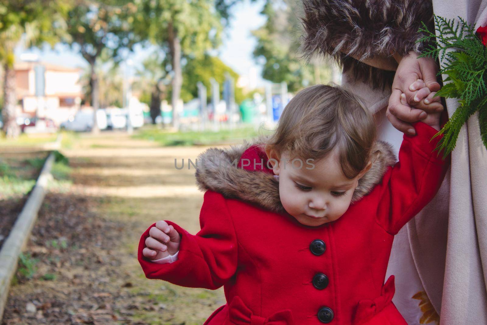 Little girl walking hand in hand with her mother on a path outdoors in a park in winter