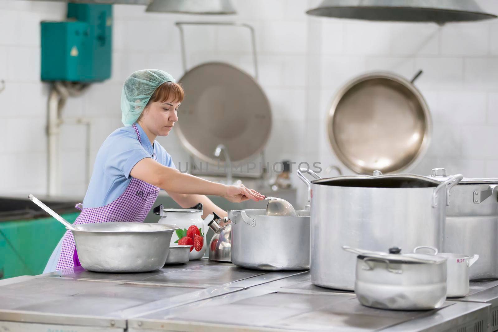 Cook prepares food. Cook with large pans and a ladle. Kitchen worker with a ladle. Worker dining.