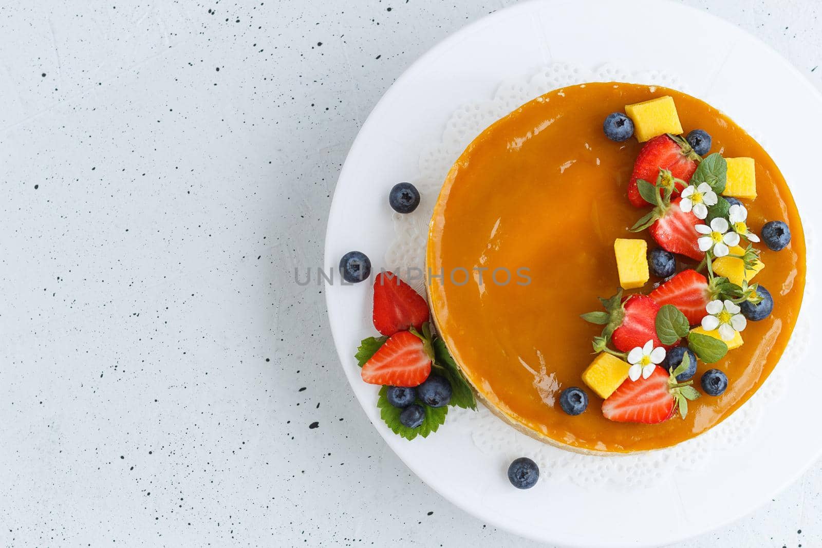 Mango cheesecake decorated with berries, mango slices and flowers on a stand. Copy space