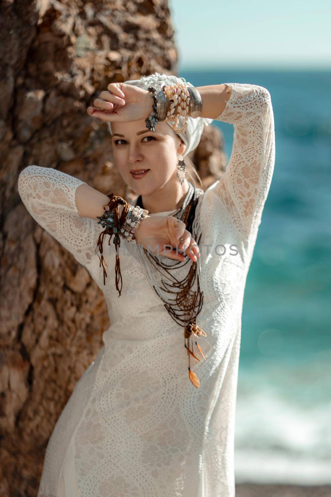 Middle aged woman looks good with blond hair, boho style in white long dress on the beach decorations on her neck and arms