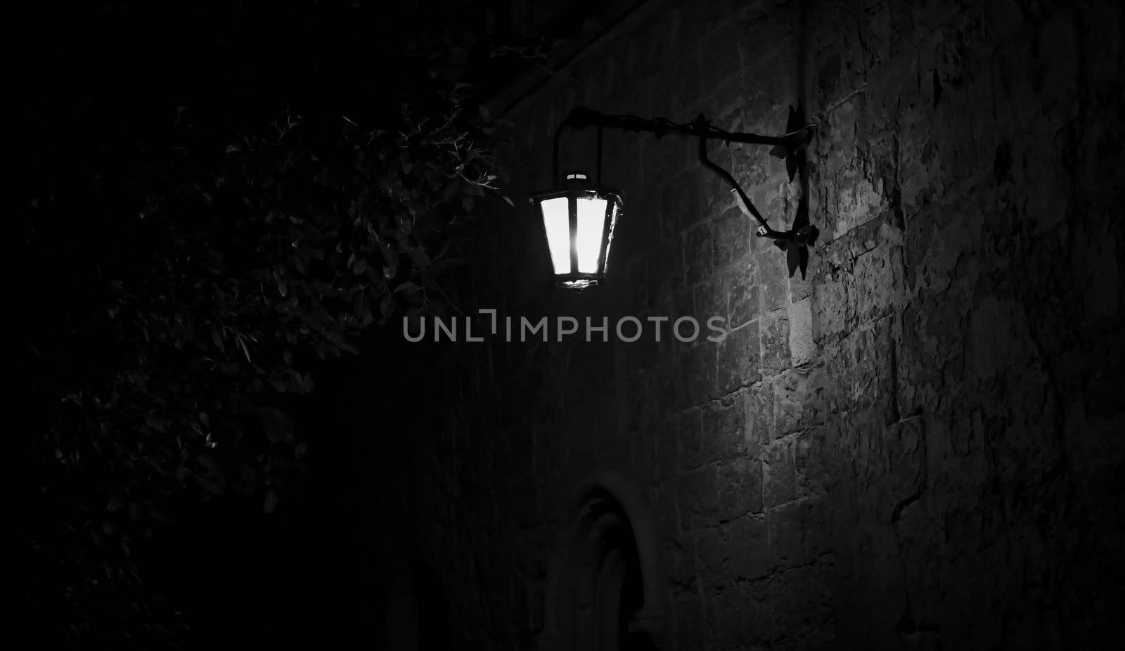 Spooky black and white alley with a lit street lamp by tennesseewitney