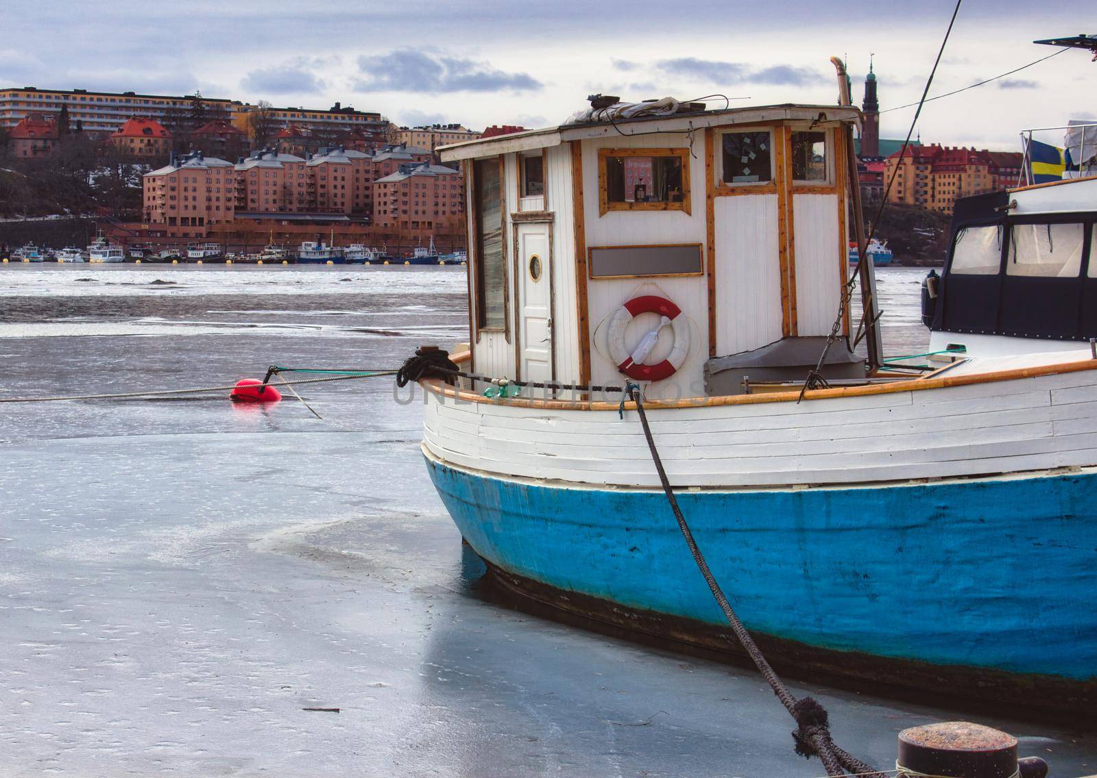 Small fishing boat with a blue hull moored on a frozen river in winter