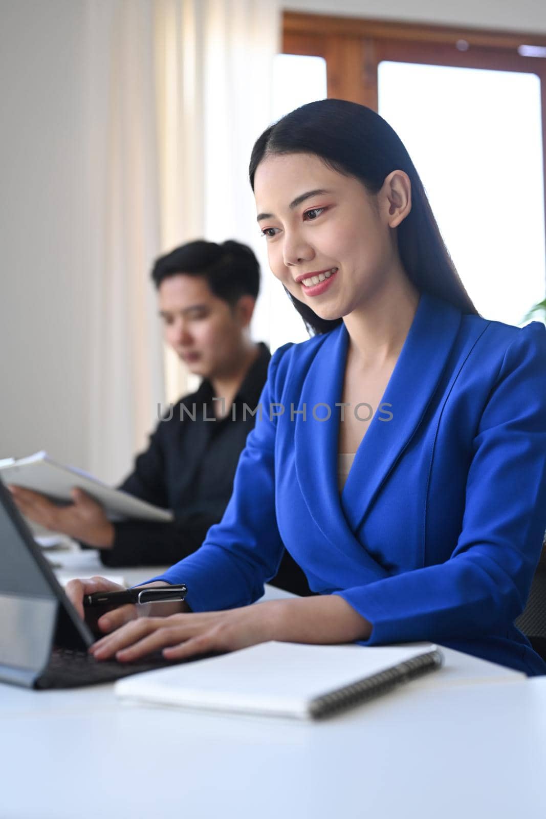 Confident business woman working with computer tablet while sitting with her colleague at office.