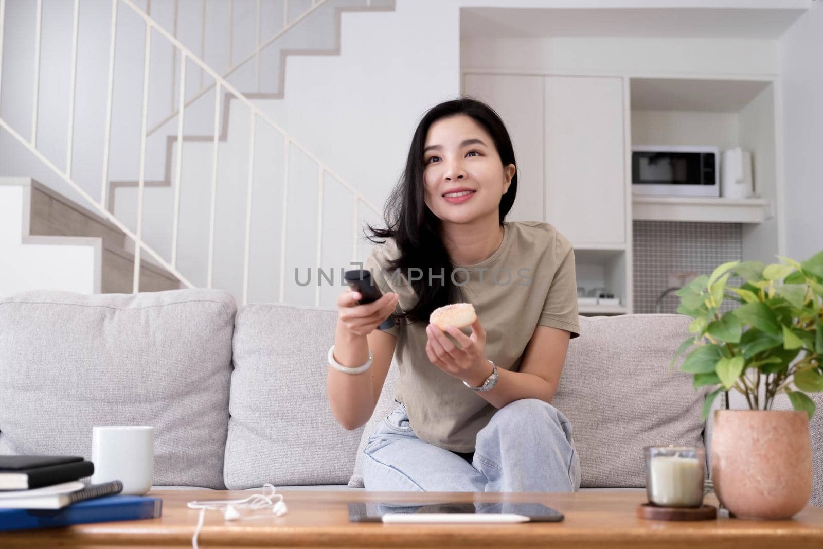 Asian young beautiful woman watching fun movie on television at home. Attractive casual girl feel happy and relax, sit on sofa having fun watch comedy video on TV in house. Activity lifestyles concept.