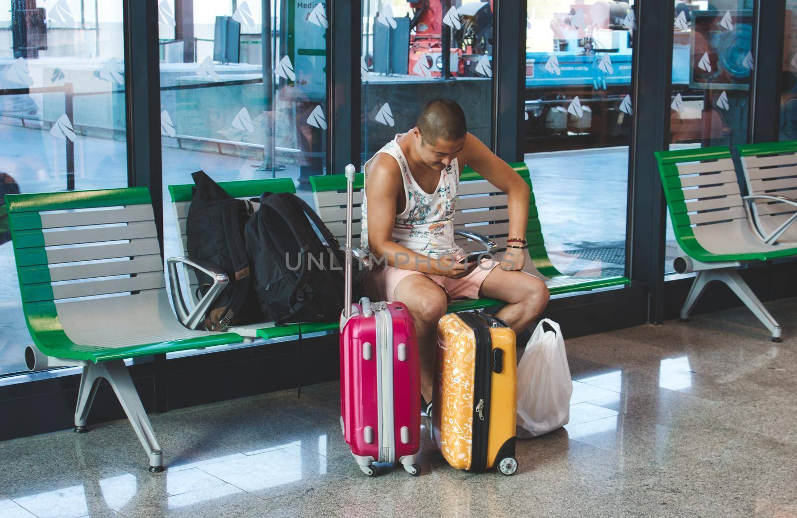 Granada / Spain - August 22 2019: A young man checking his phone at a train station with his luggage