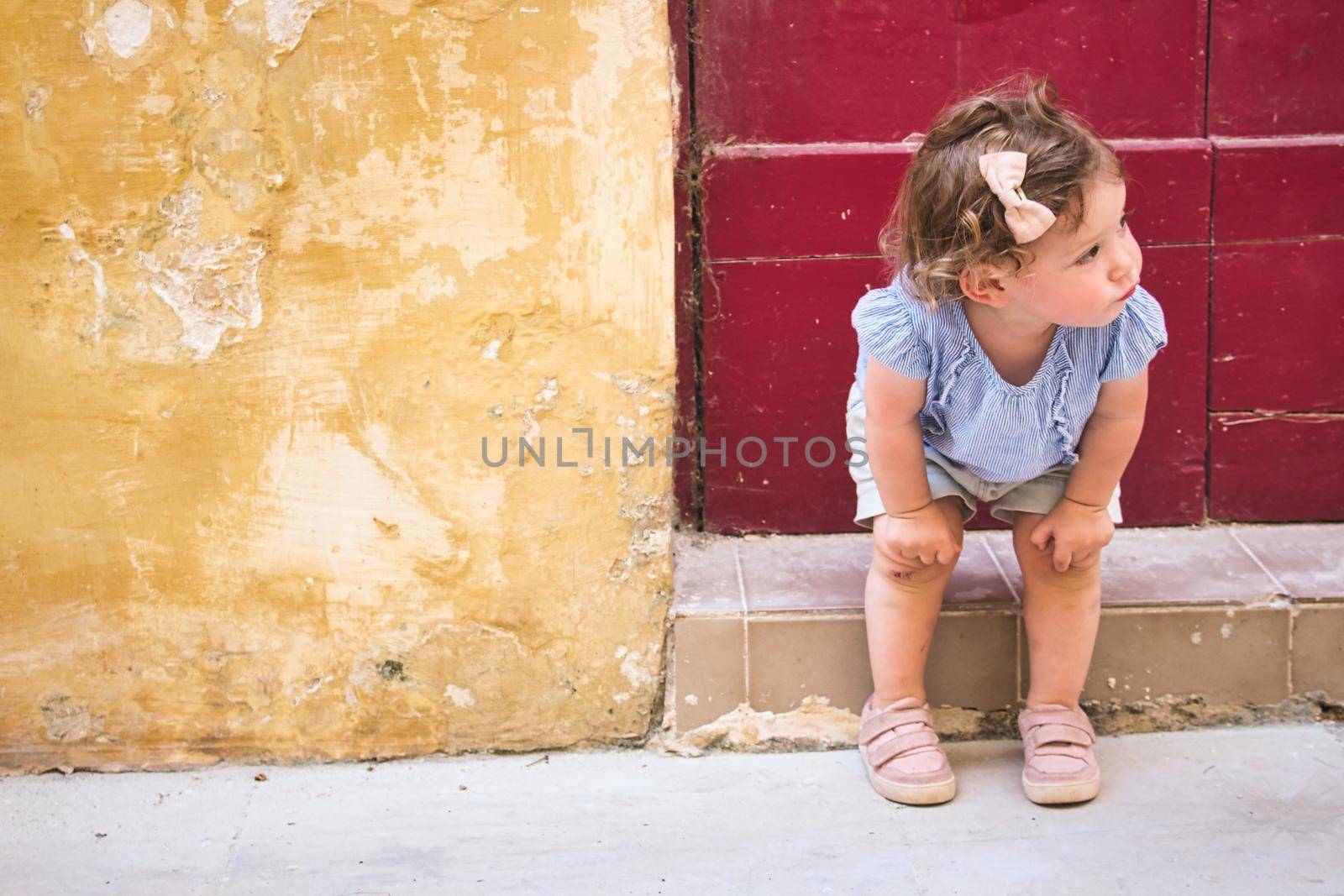 Cute baby girl sitting on the doorstep of a rural village home