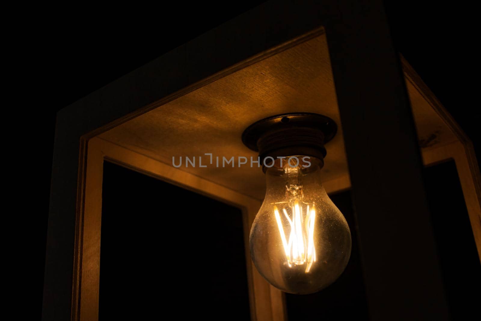 Close-up of warm yellow glowing light bulb encased in a wooden box against a black background by tennesseewitney