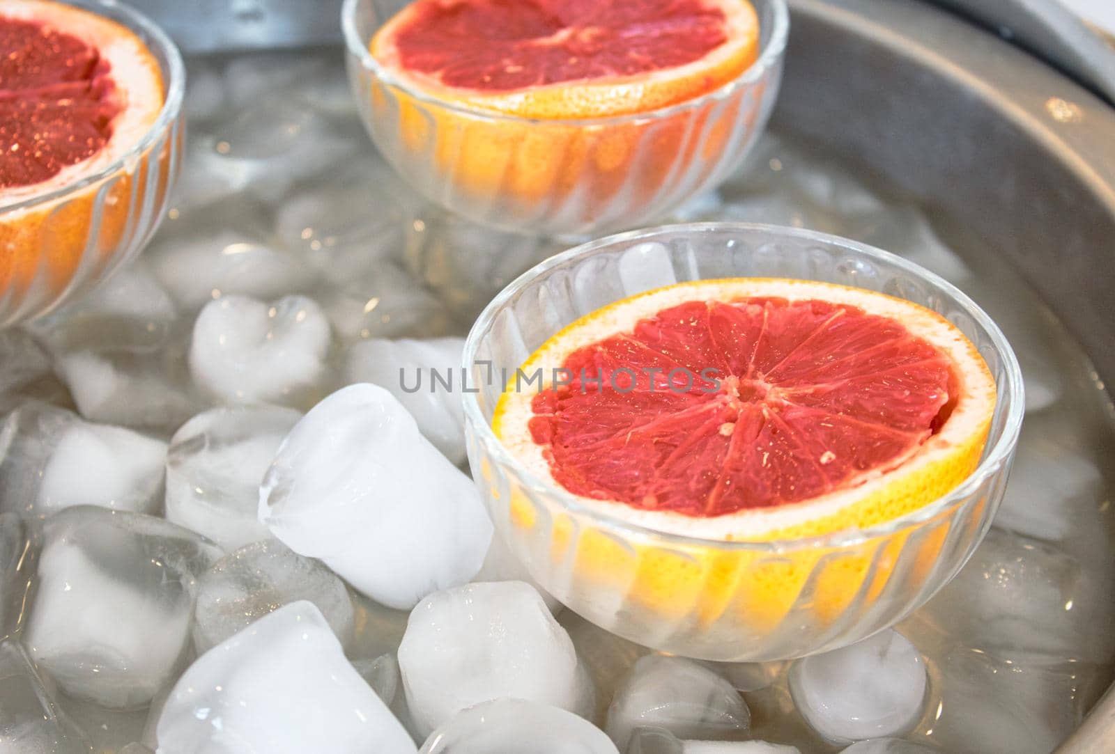 Pink grapefruit halves in glass bowls on ice