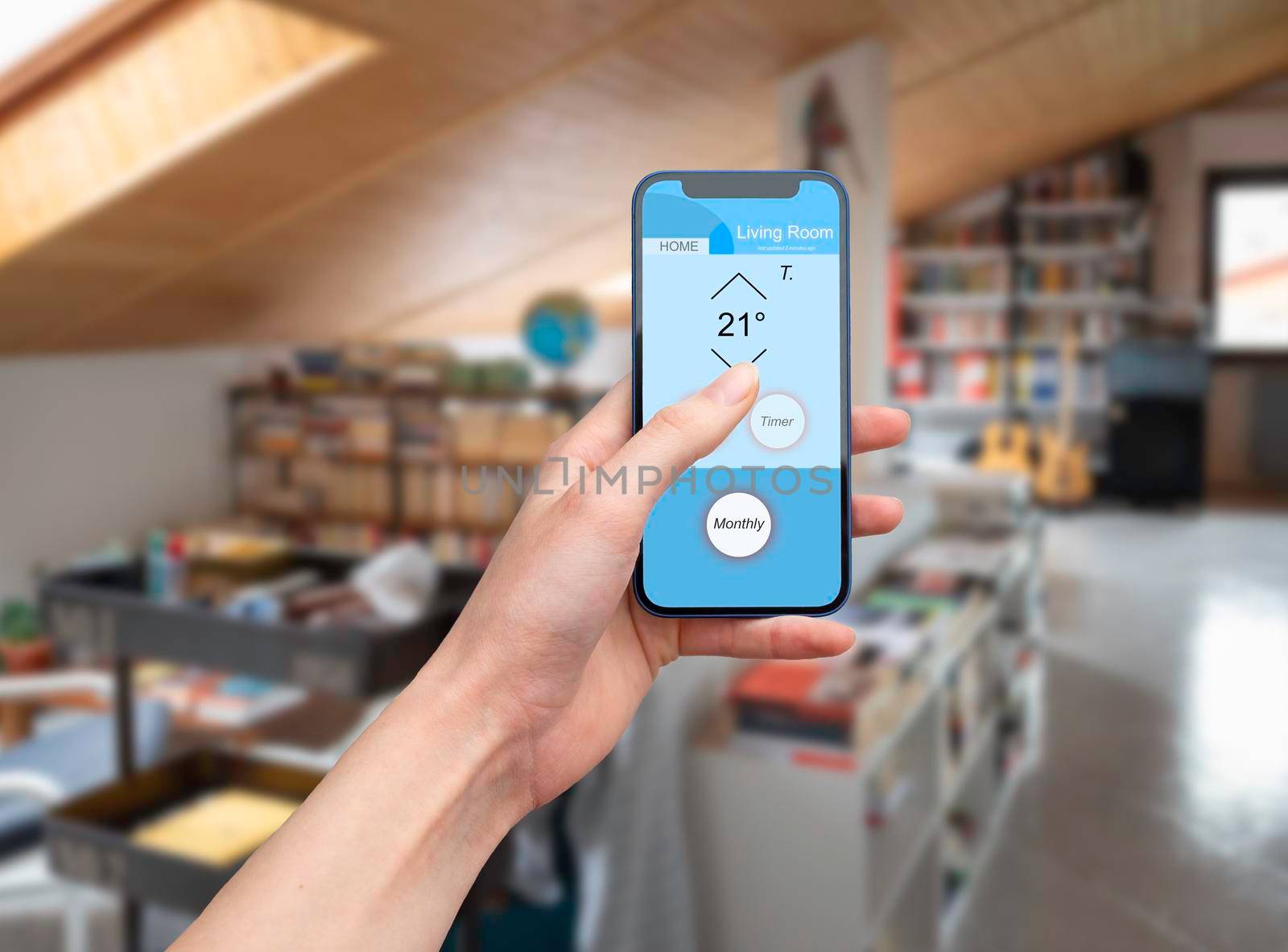 Hand holding a mobile phone showing an home automation app to manage smart technology in a modern house