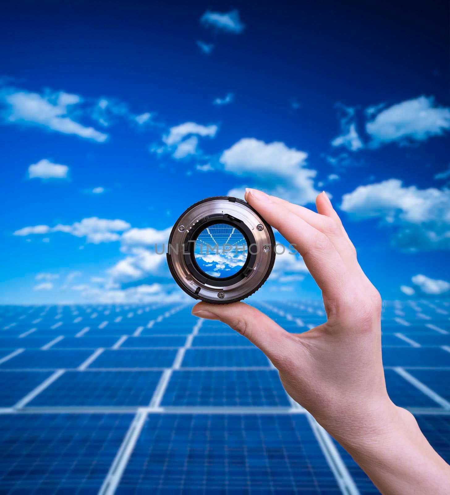 Hand holds optical lens on blue solar panels background.