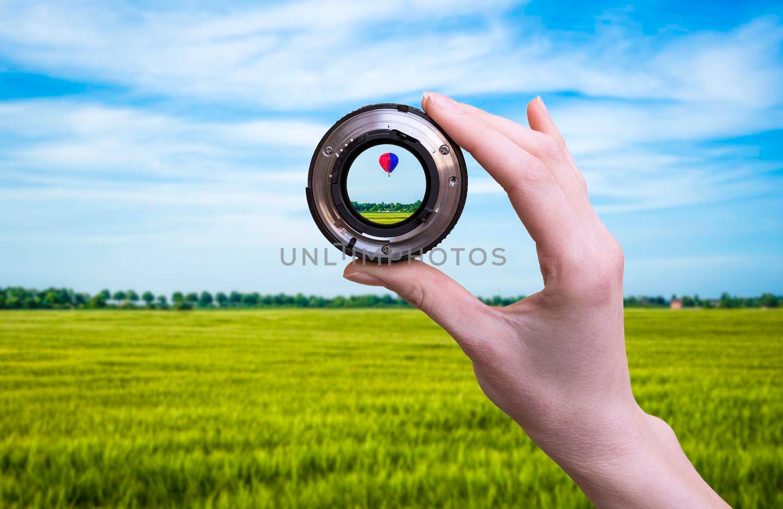 Hand holds optic lens and looking nature with hot air balloon