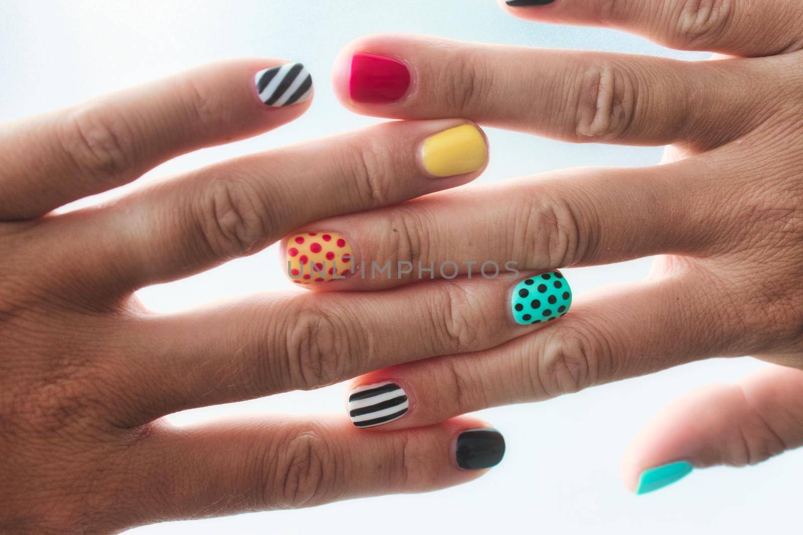 A pair of female hands with colored painted nails with different patterns