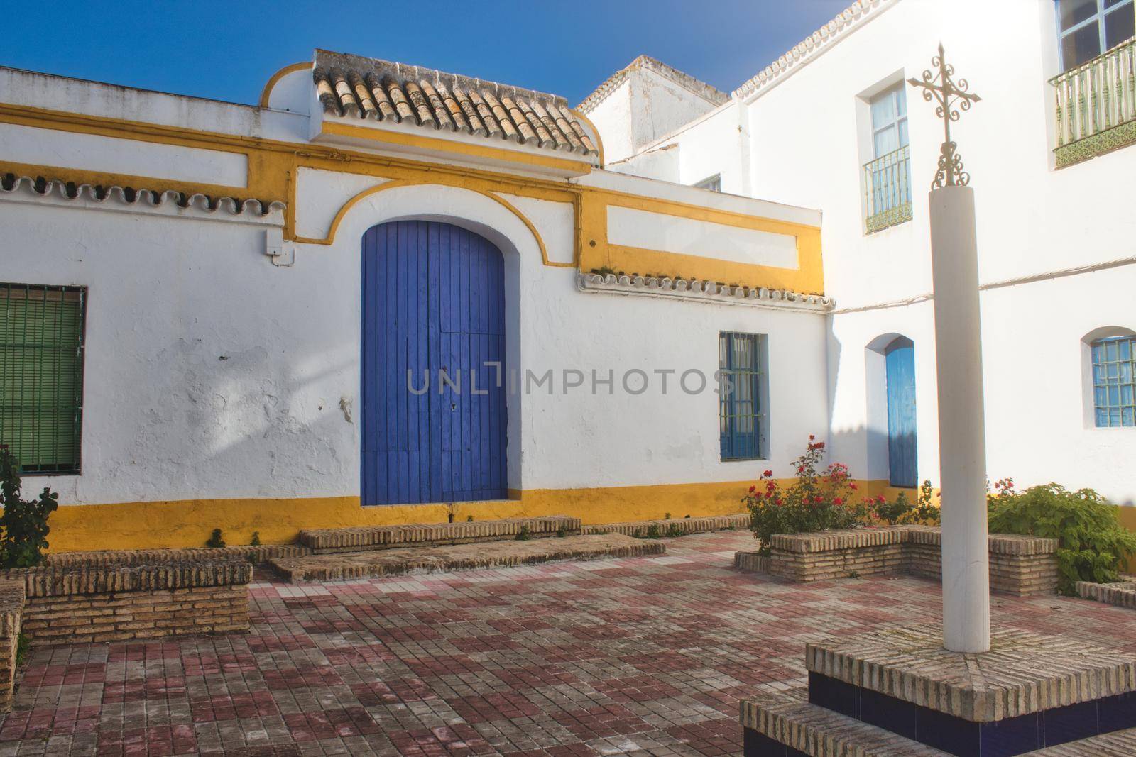 Spanish brightly colored courtyard or patio in the sun with an ornate cross on a column by tennesseewitney