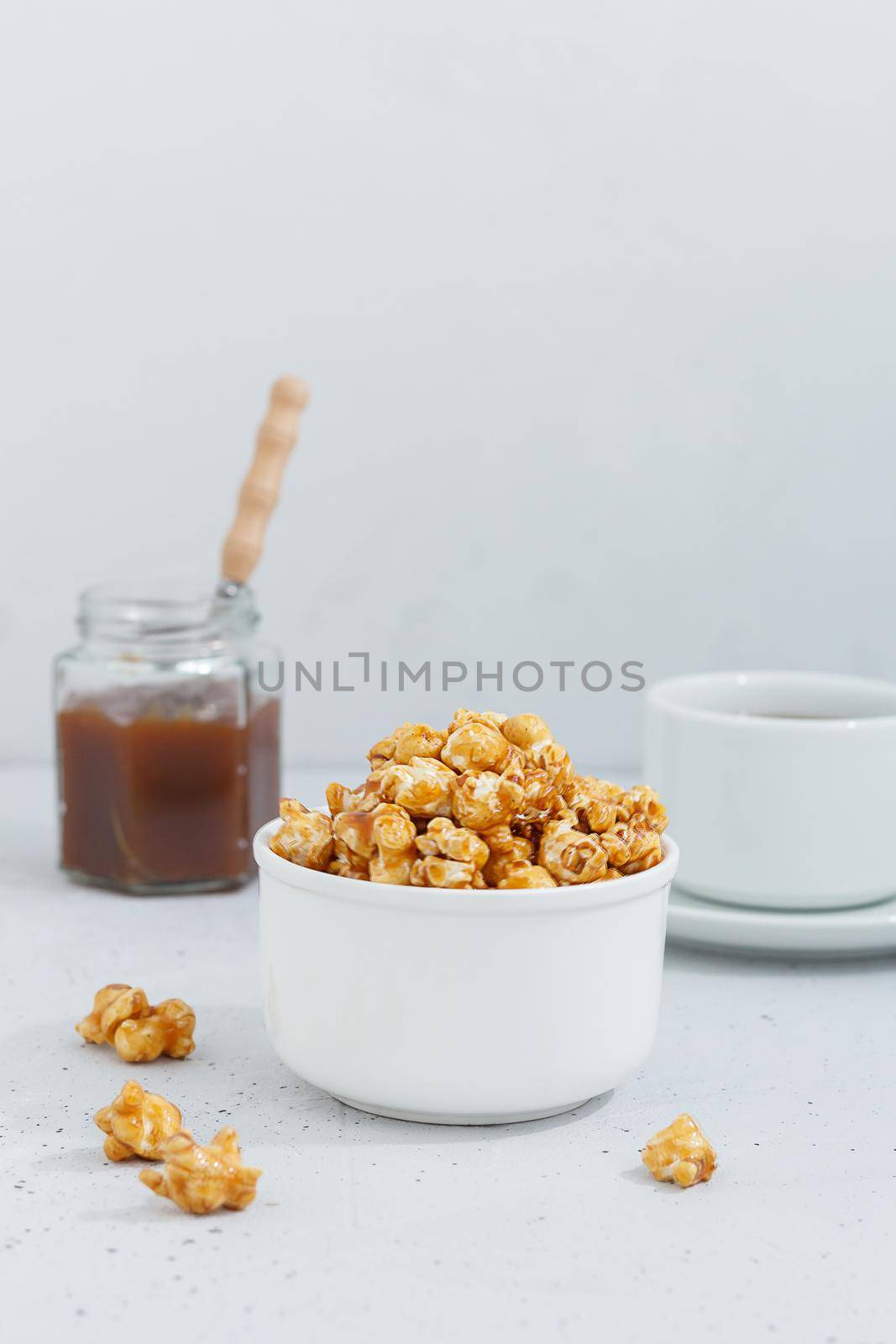 Sweet caramel popcorn in a ceramic bowl on a gray background with a jar of caramel and tea. Vertnical photo