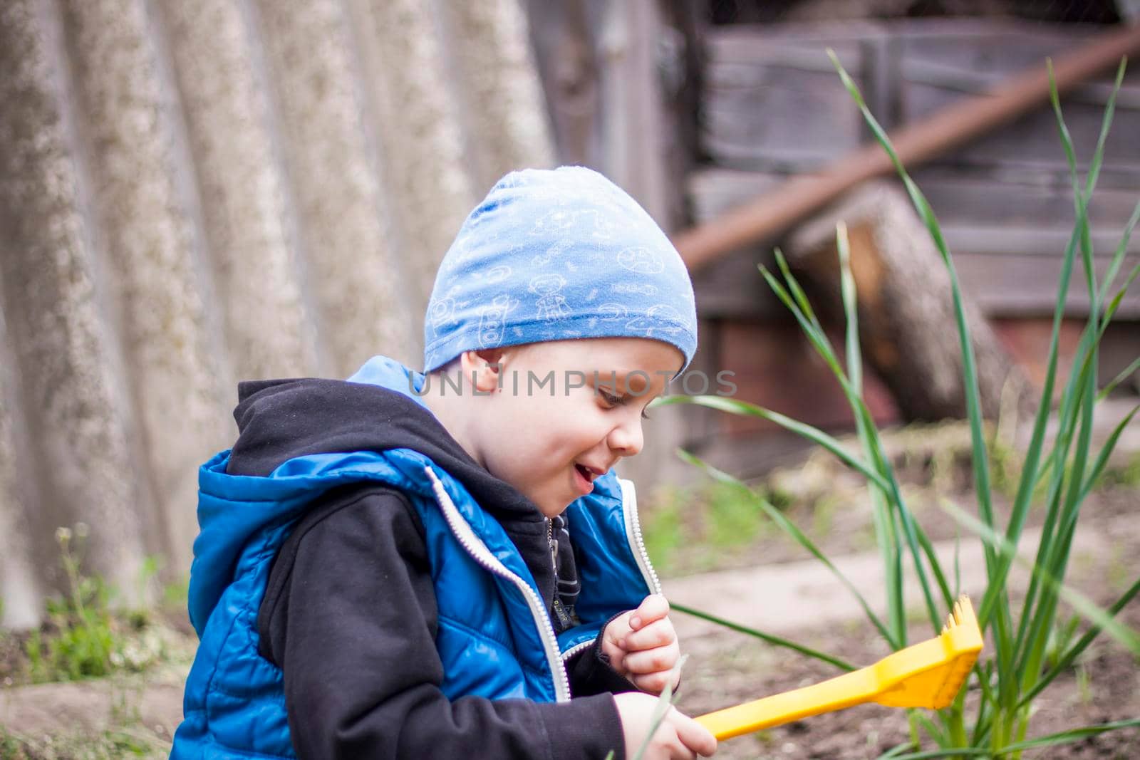 A child is planting a garden. A child's rake in his hands. A little gardener boy is planting plants in a flower bed. Gardening tools in the hands of a child. by Alina_Lebed