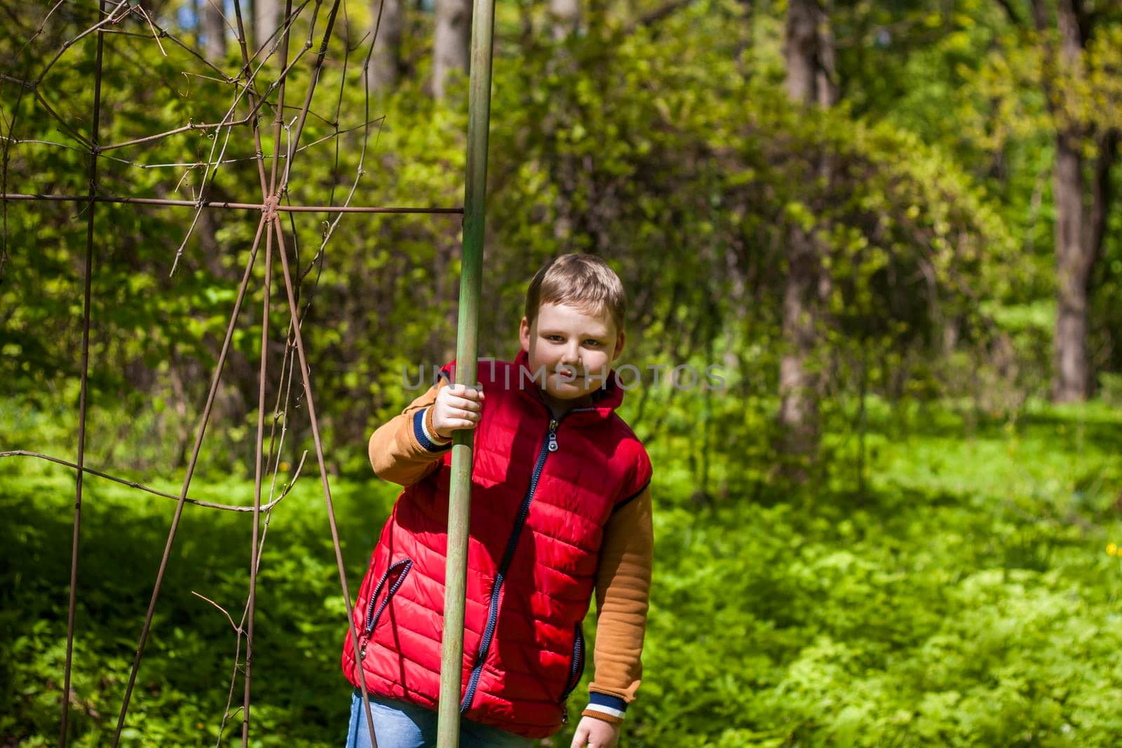 Portrait of a young man in a red tank top in the forest in spring. Walk through the green park in the fresh air. The magical light from the sun's rays falls behind the boy. Spring