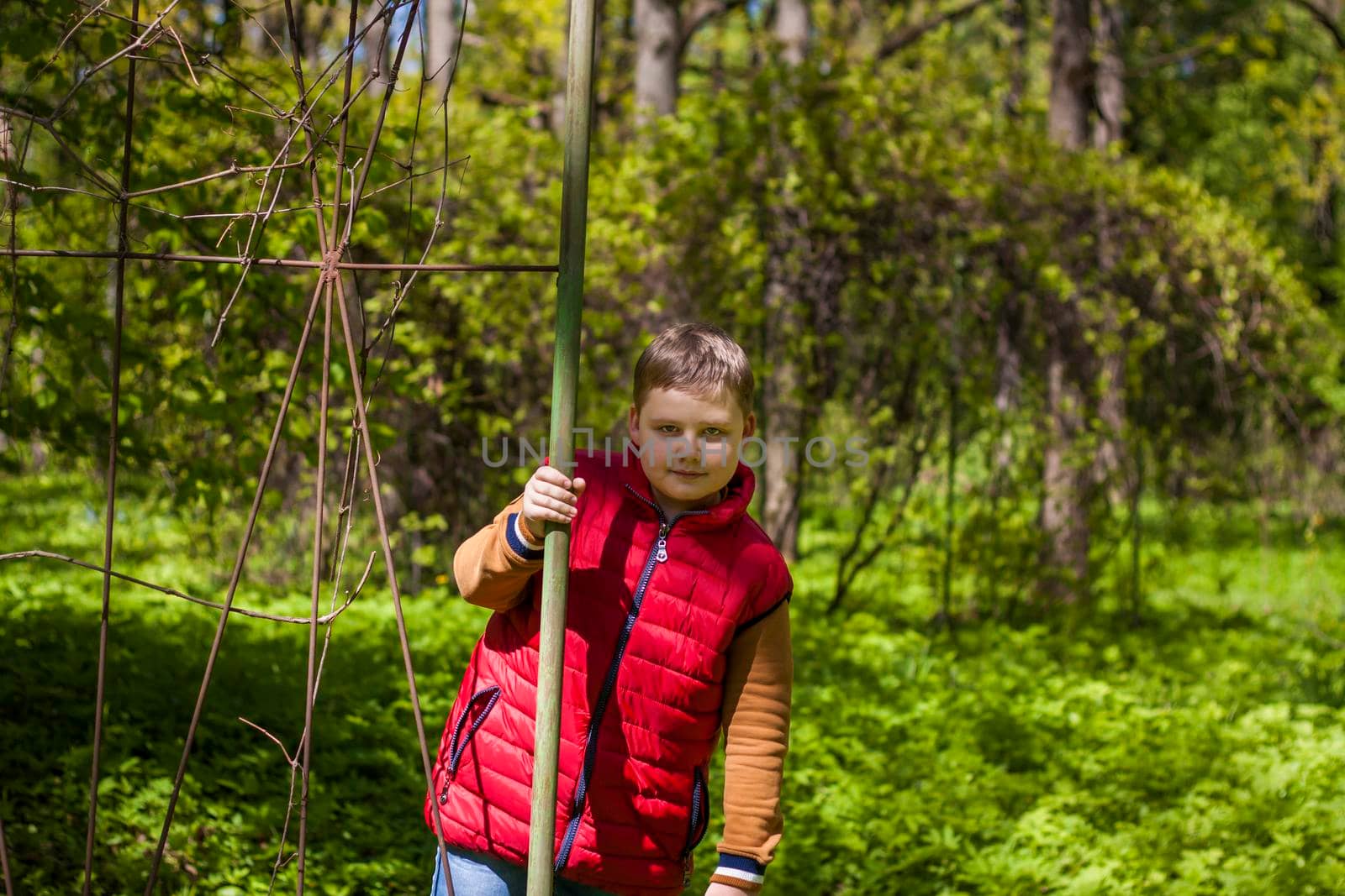 Portrait of a young man in a red tank top in the forest in spring. Walk through the green park in the fresh air. The magical light from the sun's rays falls behind the boy. Spring