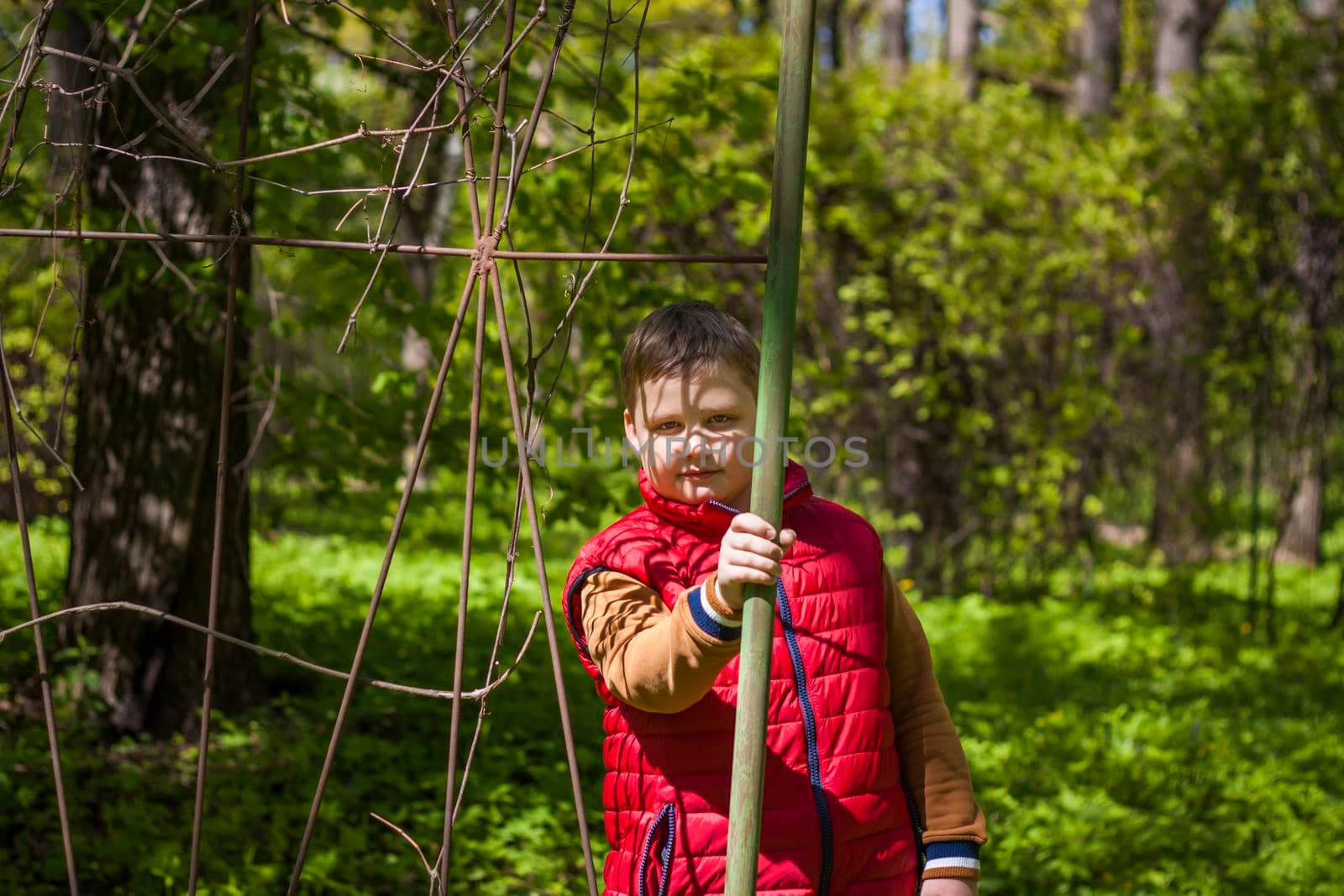 Portrait of a young man in a red tank top in the forest in spring. Walk through the green park in the fresh air. The magical light from the sun's rays falls behind the boy. Spring