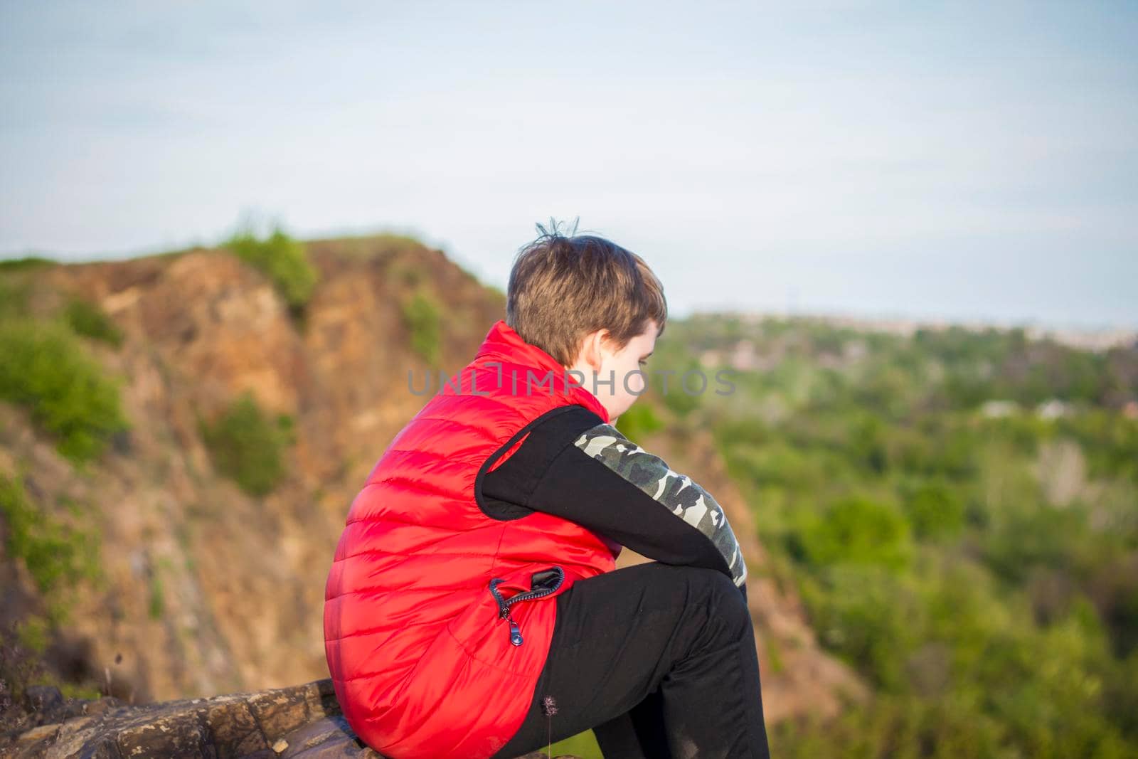 A child sits on top of a cliff and watches what is happening below. panoramic view from the top of a rocky mountain. Russia, Rostov region, skelevataya skala, the 7th wonder of the Don world. Landscape