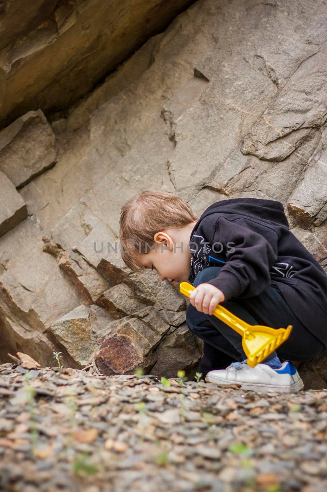 A boy-child on the background of a rocky mountain looks at something with curiosity and is surprised. Nature, rocks, mountains. Portrait of a cute boy outdoors.