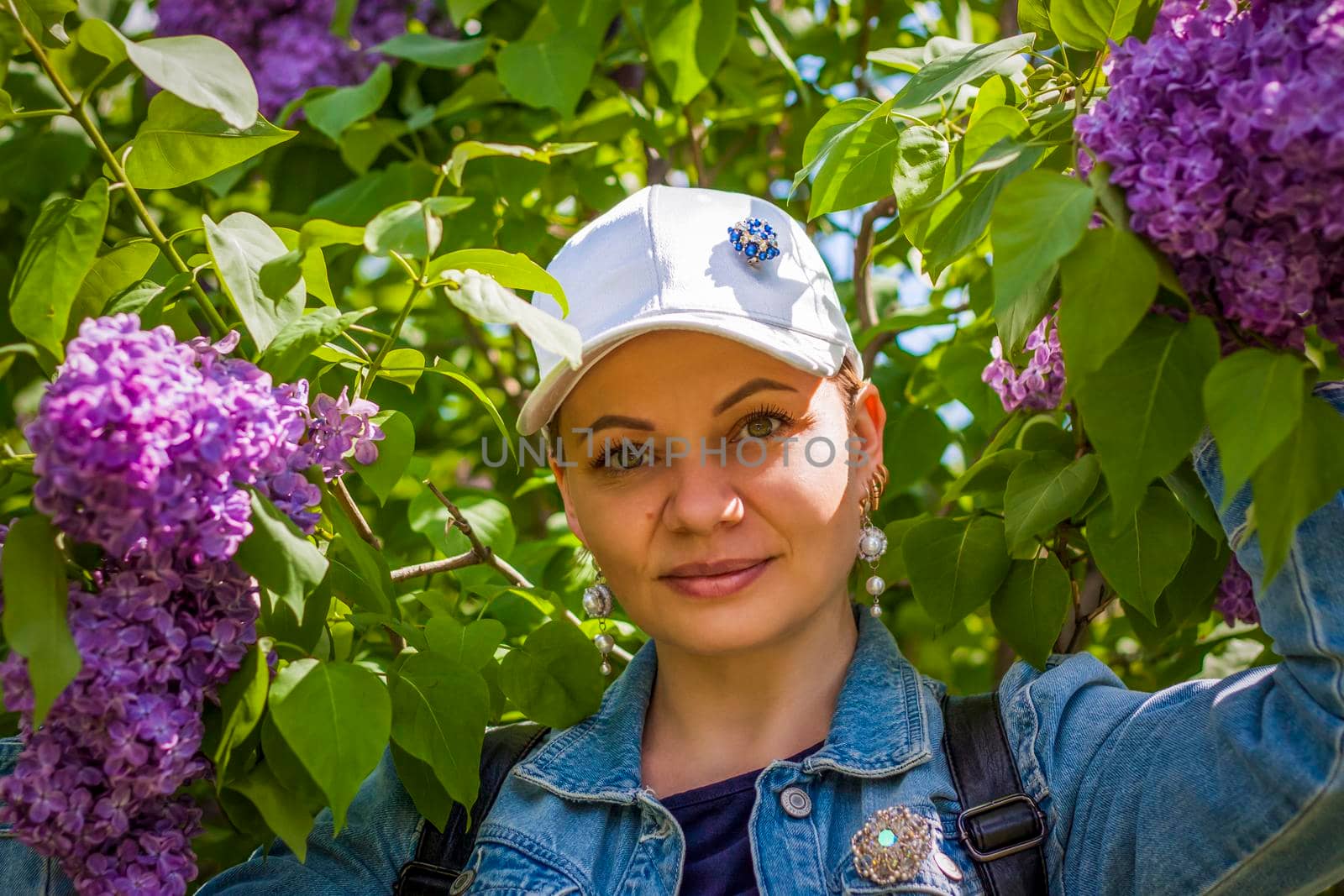 A young woman in a white cap poses near a lilac bush. Portrait of a girl. Interactions. Selective focus. Spring