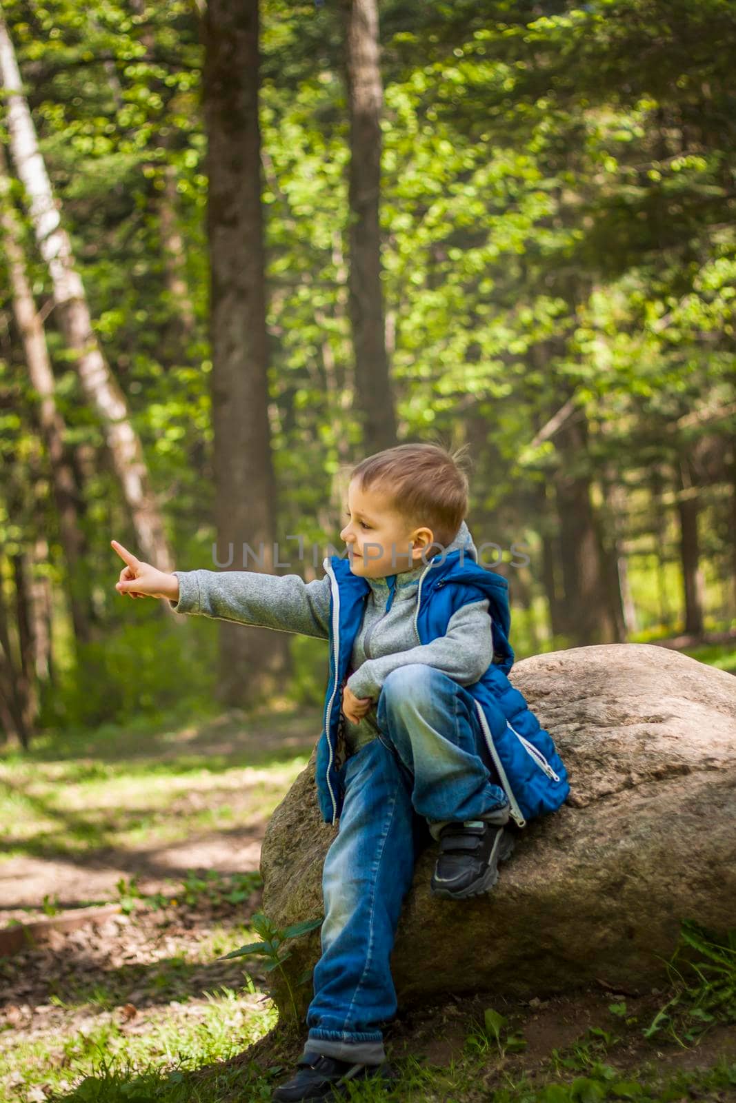 Portrait of a boy in a blue tank top in the woods in spring. Take a walk in the green park in the fresh air. The magical light from the sun's rays falls behind the boy. Spring