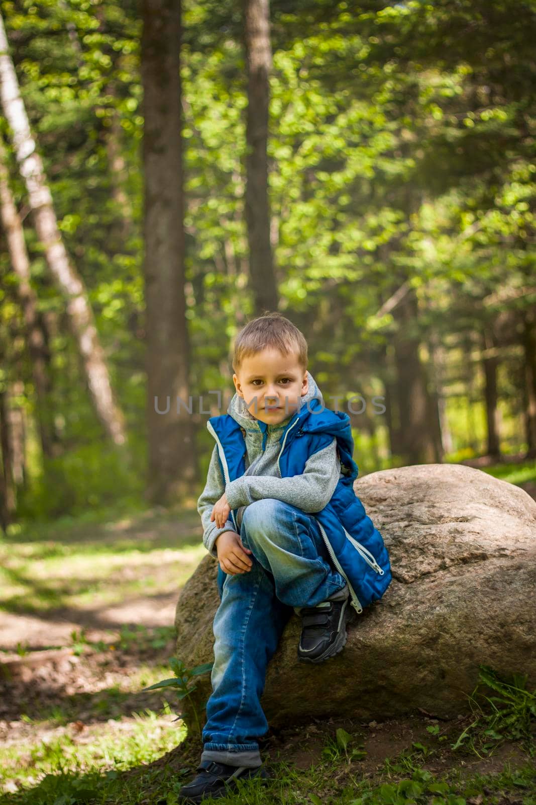 Portrait of a boy in a blue tank top in the woods in spring. Take a walk in the green park in the fresh air. The magical light from the sun's rays falls behind the boy. Spring