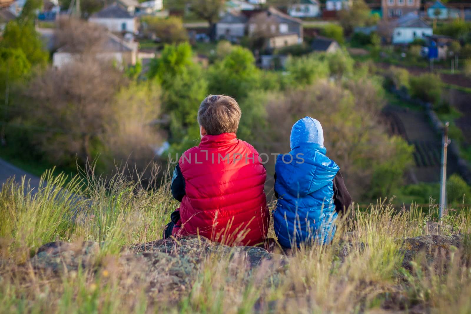 Children sit on top of a cliff and watch what is happening below. View from the back. panoramic view from above. Russia, Rostov region, skelevataya skala, the 7th wonder of the Don world. Landscape