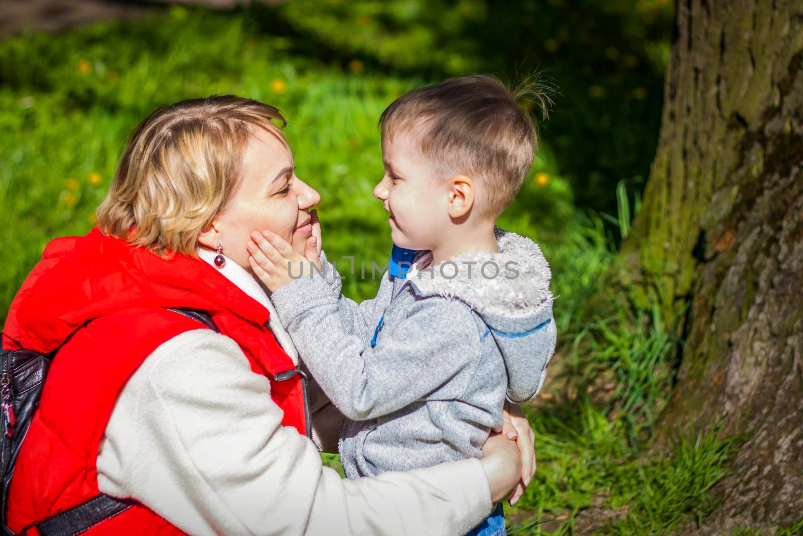 Children with their mother pose in a sunny clearing near a tree in the forest. The sun's rays envelop the space. Interaction history. Space for copying. Selective focus.