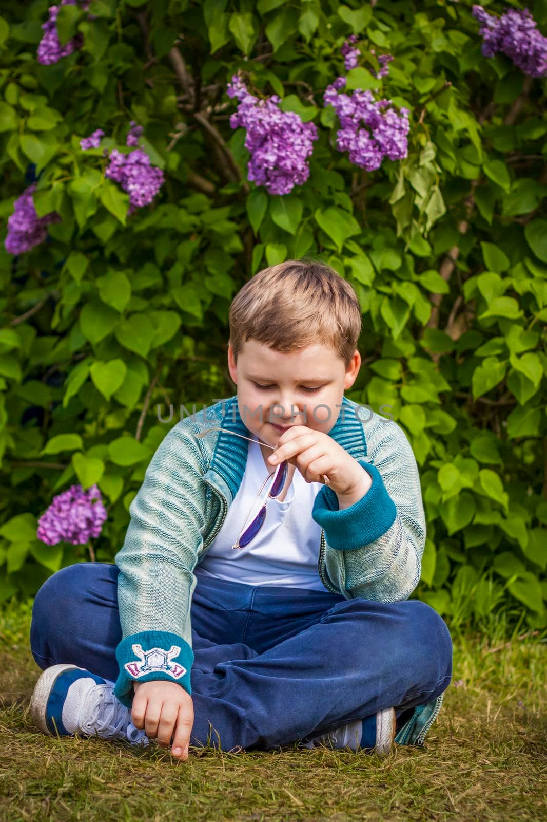 A boy poses near a lush lilac. Portrait of children with an interesting facial expression. Interactions. Selective focus. Spring