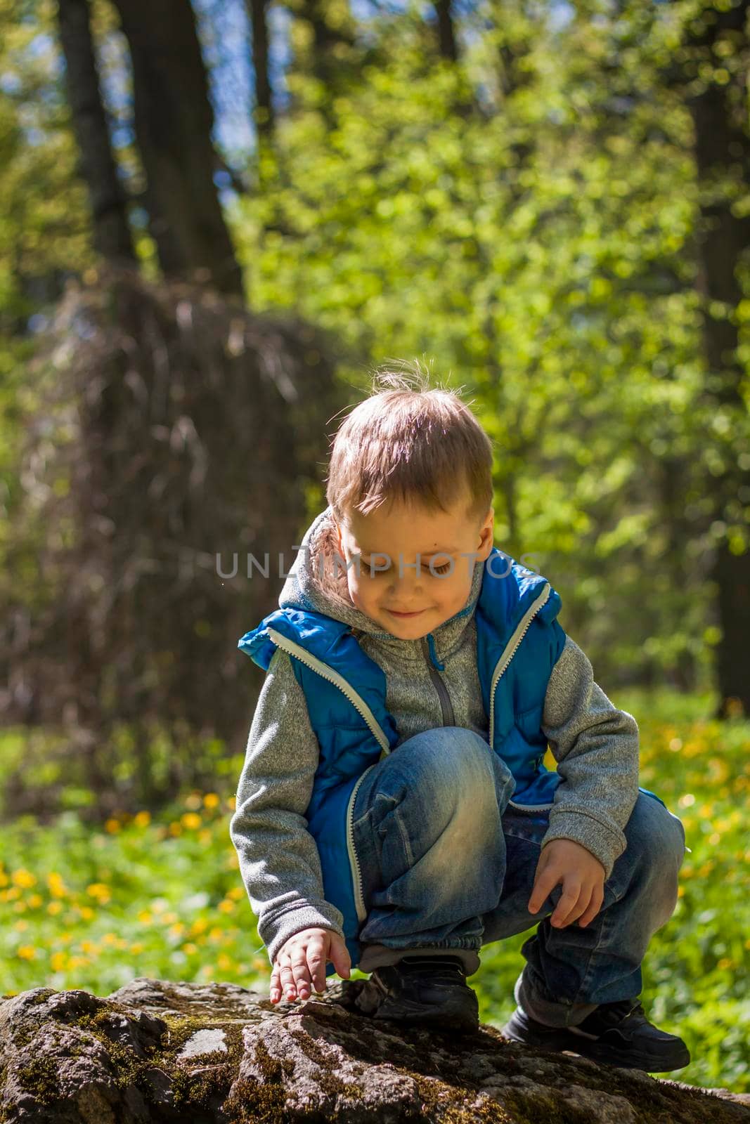 Portrait of a boy in a blue tank top in the woods in spring. Take a walk in the green park in the fresh air. The magical light from the sun's rays falls behind the boy. Spring