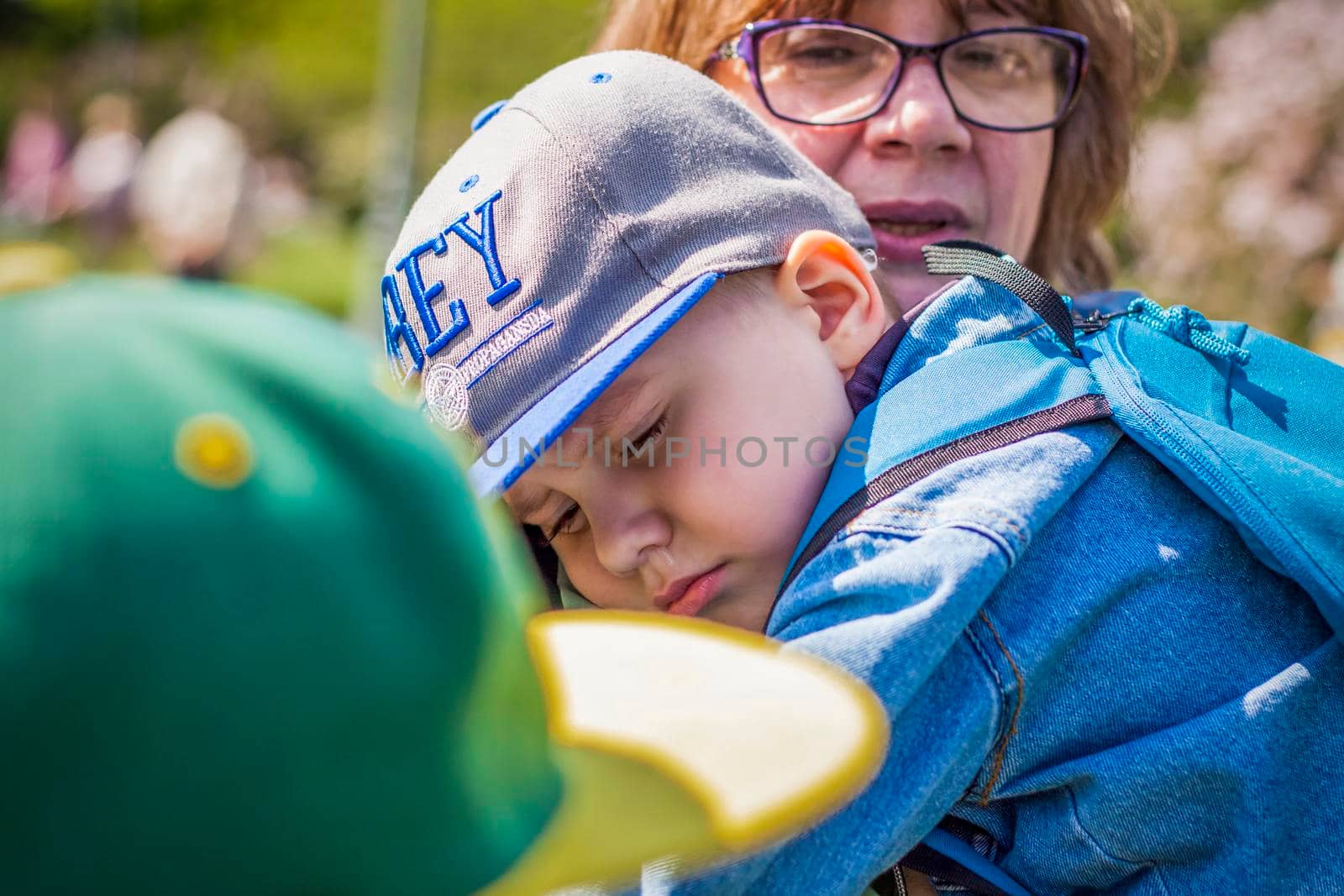 A moody child cuddles up to his young grandmother in the park. The woman feels sorry for the boy in her arms. Interactions. Selective focus. by Alina_Lebed