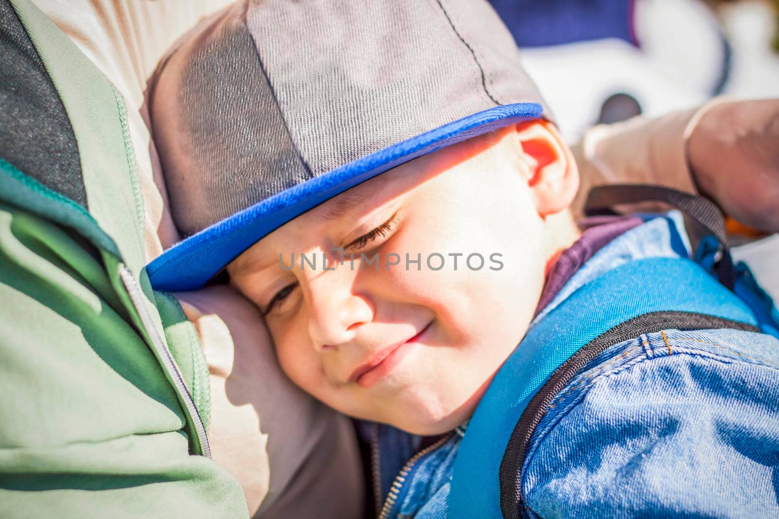 A moody child cuddles up to his young grandmother in the park. The woman feels sorry for the boy in her arms. Interactions. Selective focus. Spring