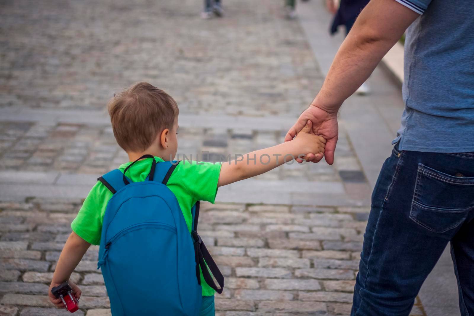 A father holds his son's hand while walking down a city street.  Travel. Lifestyle in the city. Center, streets. Summer, a walk.