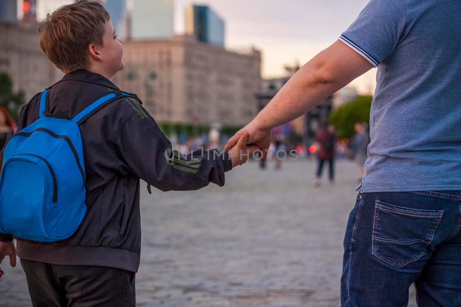 A father holds his son's hand while walking down a city street.  Travel. Lifestyle in the city. Center, streets. by Alina_Lebed