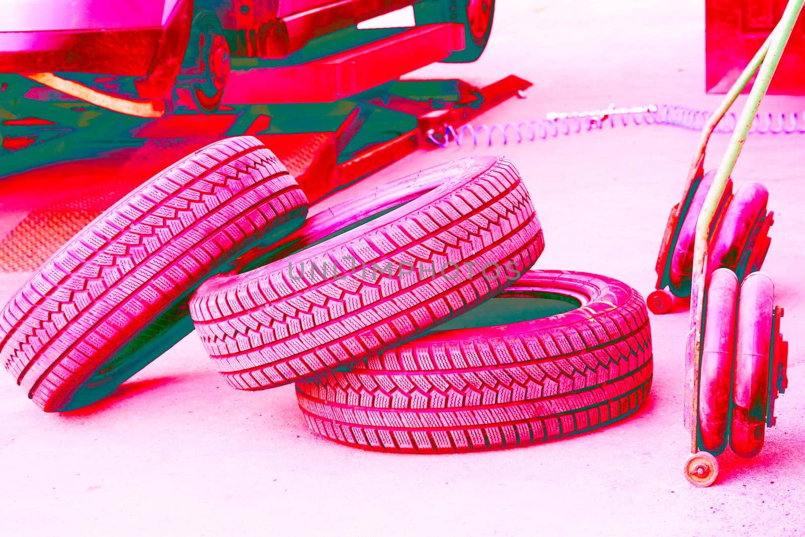 Pink magenta neon replacing a car wheel at a tire station. a rubber covering, typically inflated or surrounding an inflated inner tube, placed around a wheel to form a flexible contact with the road.