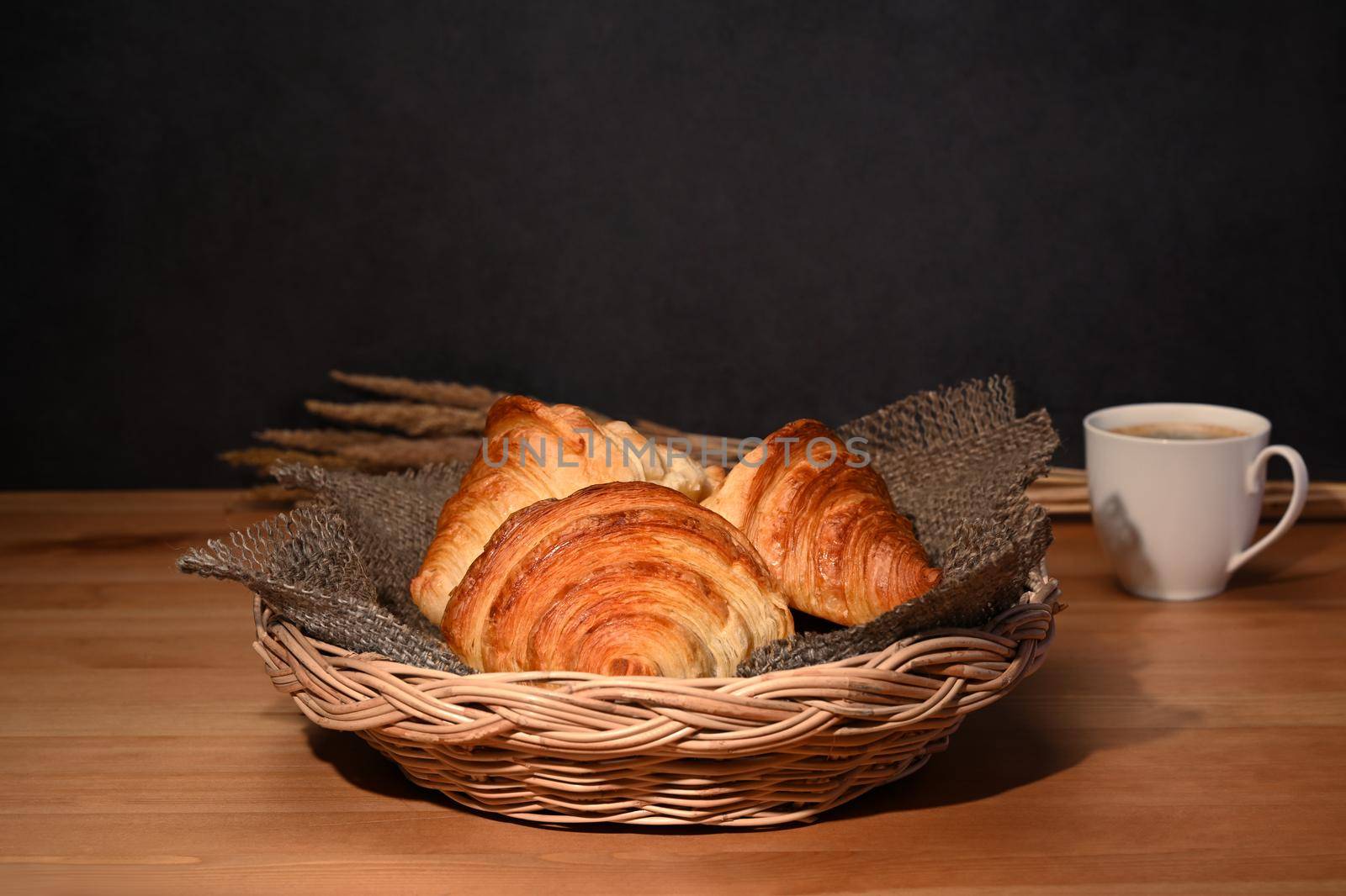 Warm fresh buttery croissants in wicker basket. Breakfast, bread bakery products cafe concept.