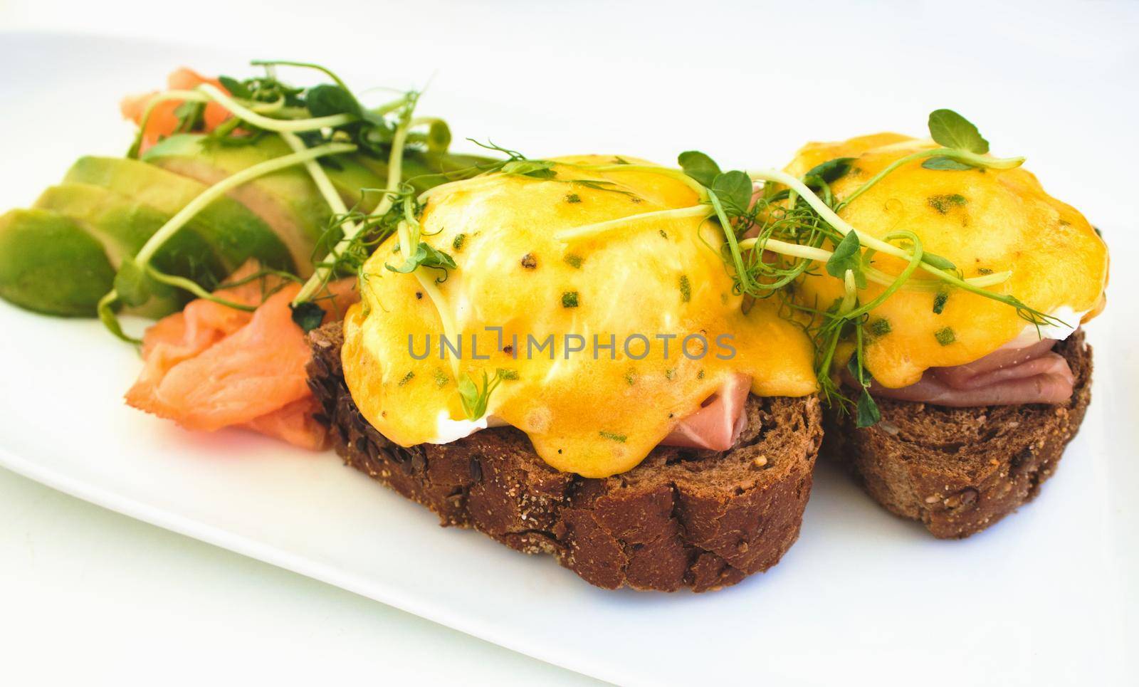 Eggs Benedict on brown bread toast with smoked salmon and sliced avocado by tennesseewitney