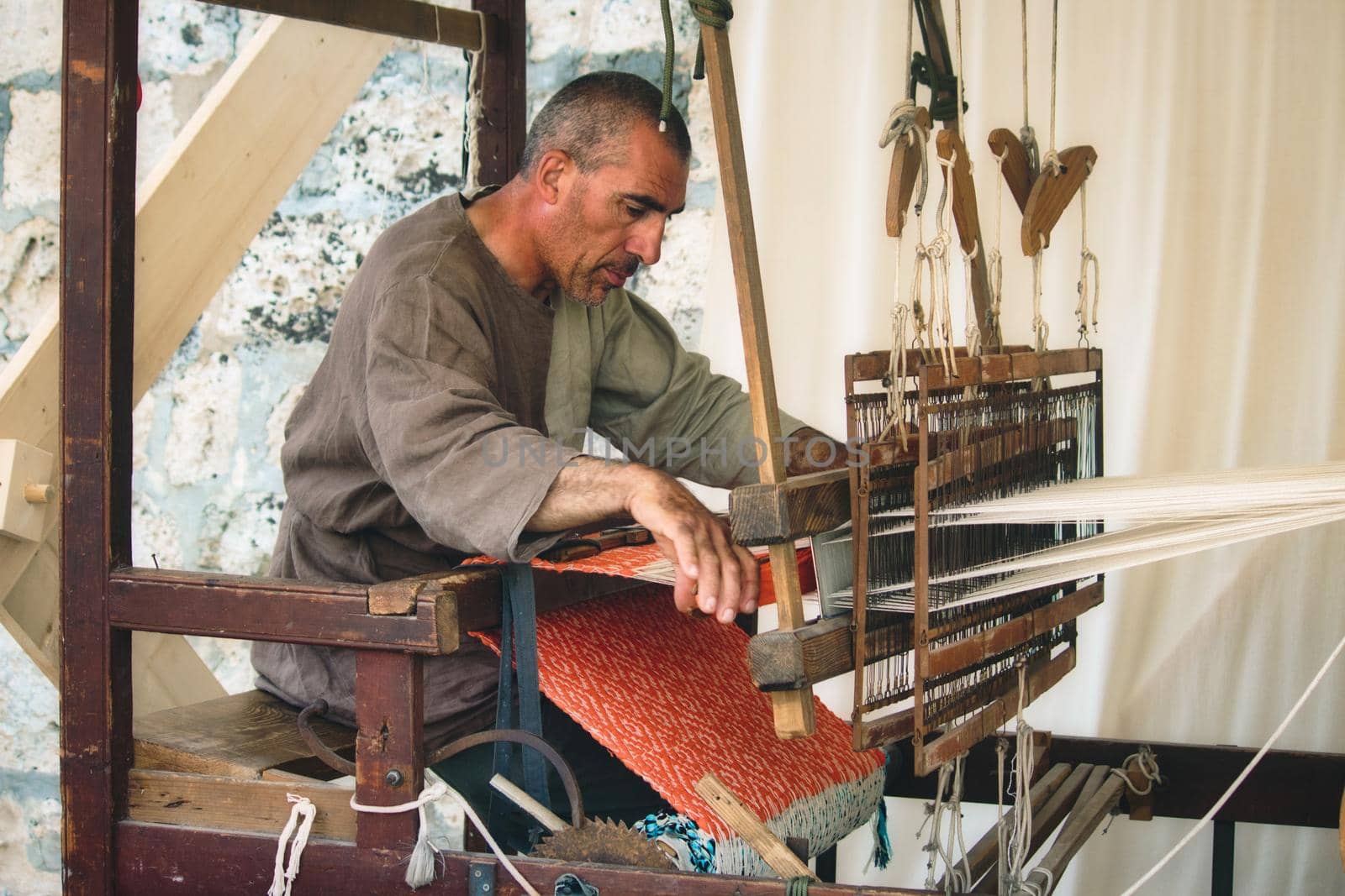 MDINA / MALTA - MAY 04 2019: Man using a foot-treadle floor loom to weave cloth by tennesseewitney