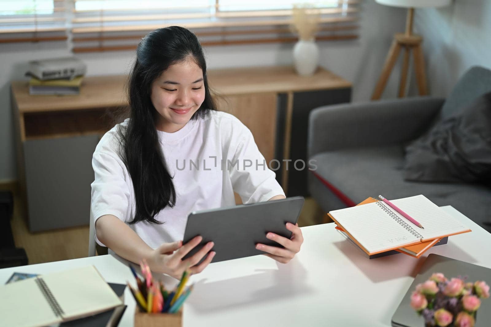 Smiling female student working or studying online on digital tablet at home.