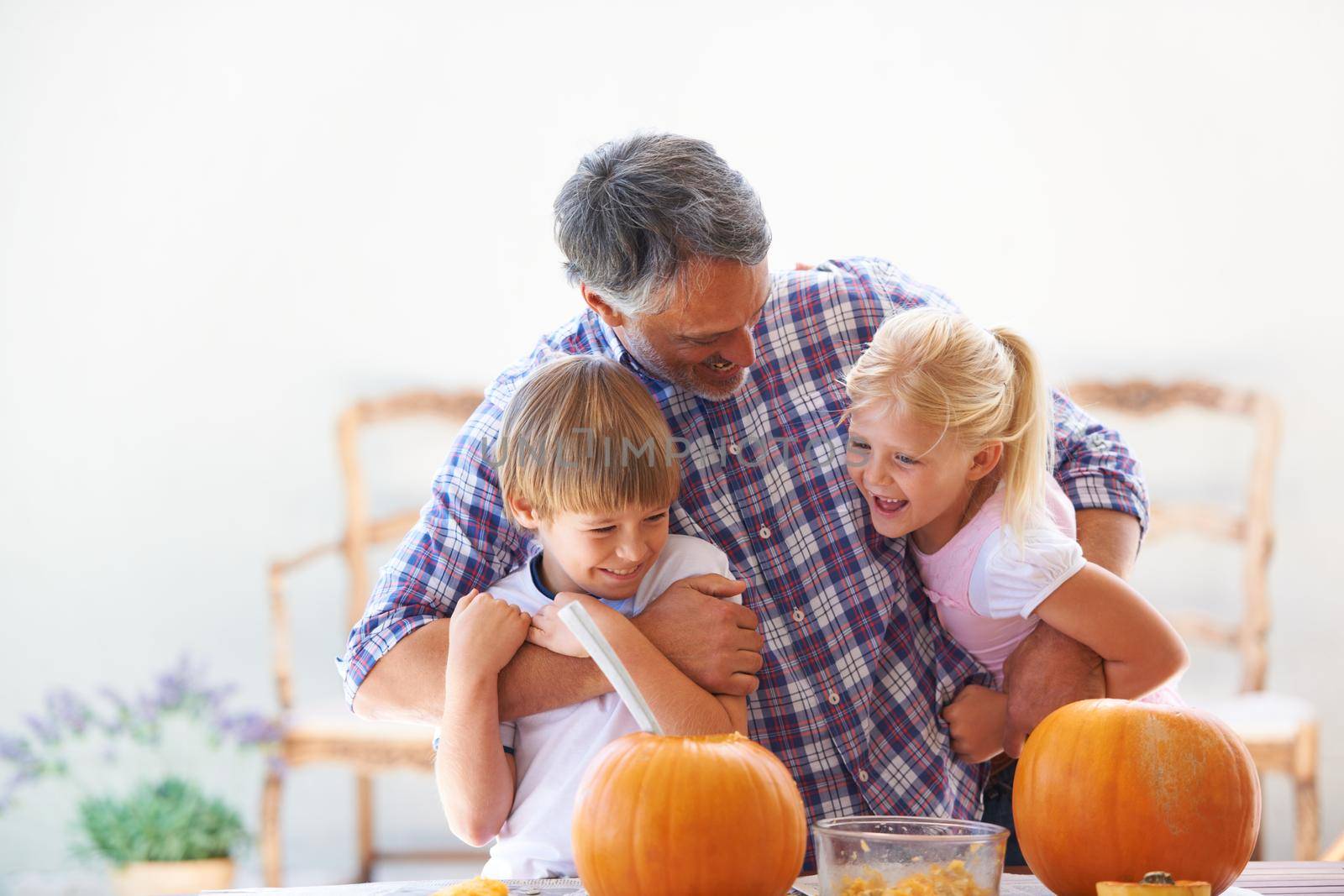 He loves spending time with his kids. A father embracing his son and daughter while hollowing out pumpkins for halloween. by YuriArcurs